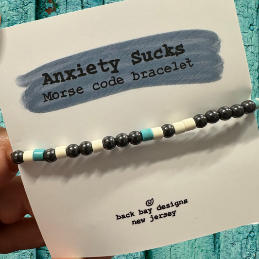 Beaded bracelet labeled 'Anxiety Sucks Morse code bracelet' on a card with text.