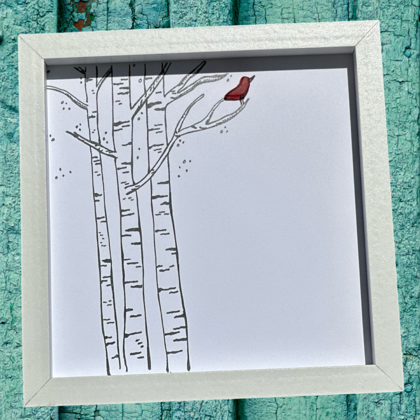 A framed seaglass art piece depicting a birch tree with a red bird perched on a branch, encased in a shadowbox frame.