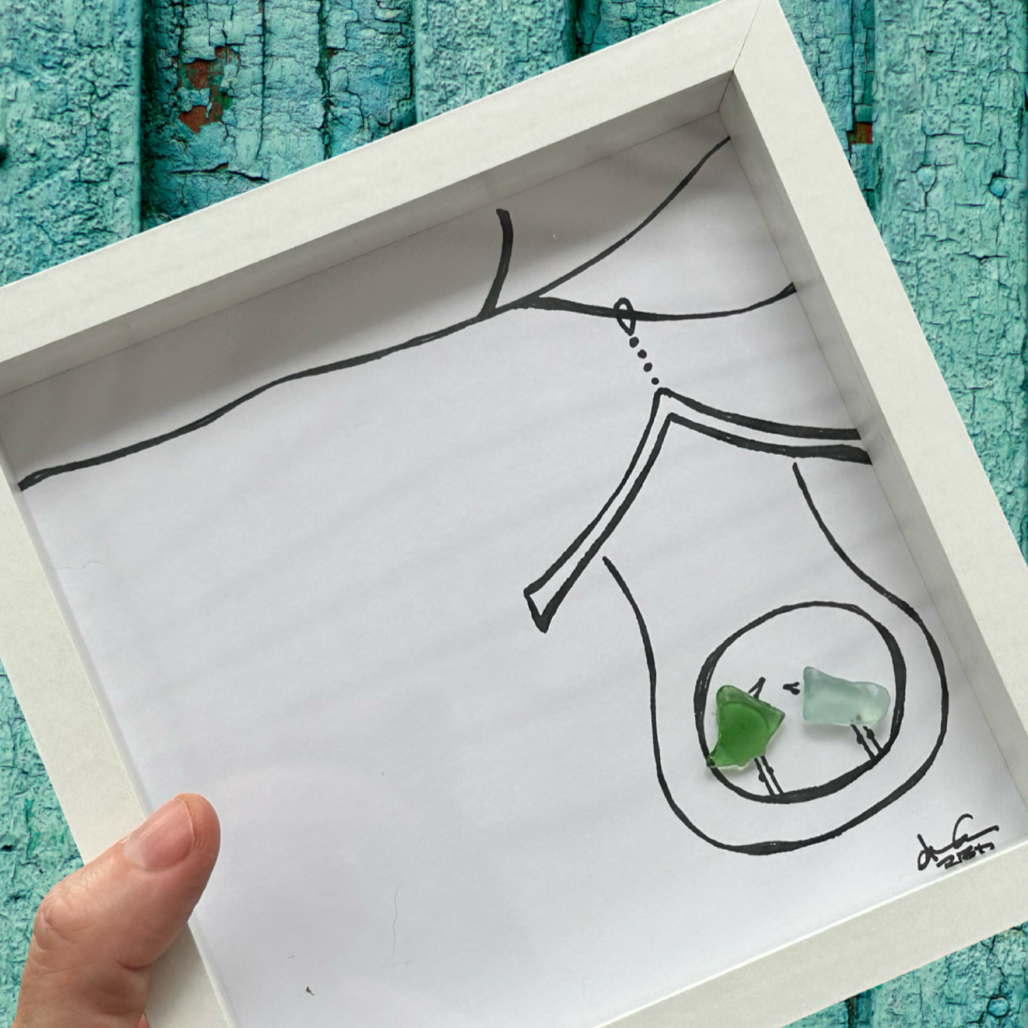 A hand holding a 6x6 seaglass art birdhouse with a drawing of a seagull inside. Sea glass art