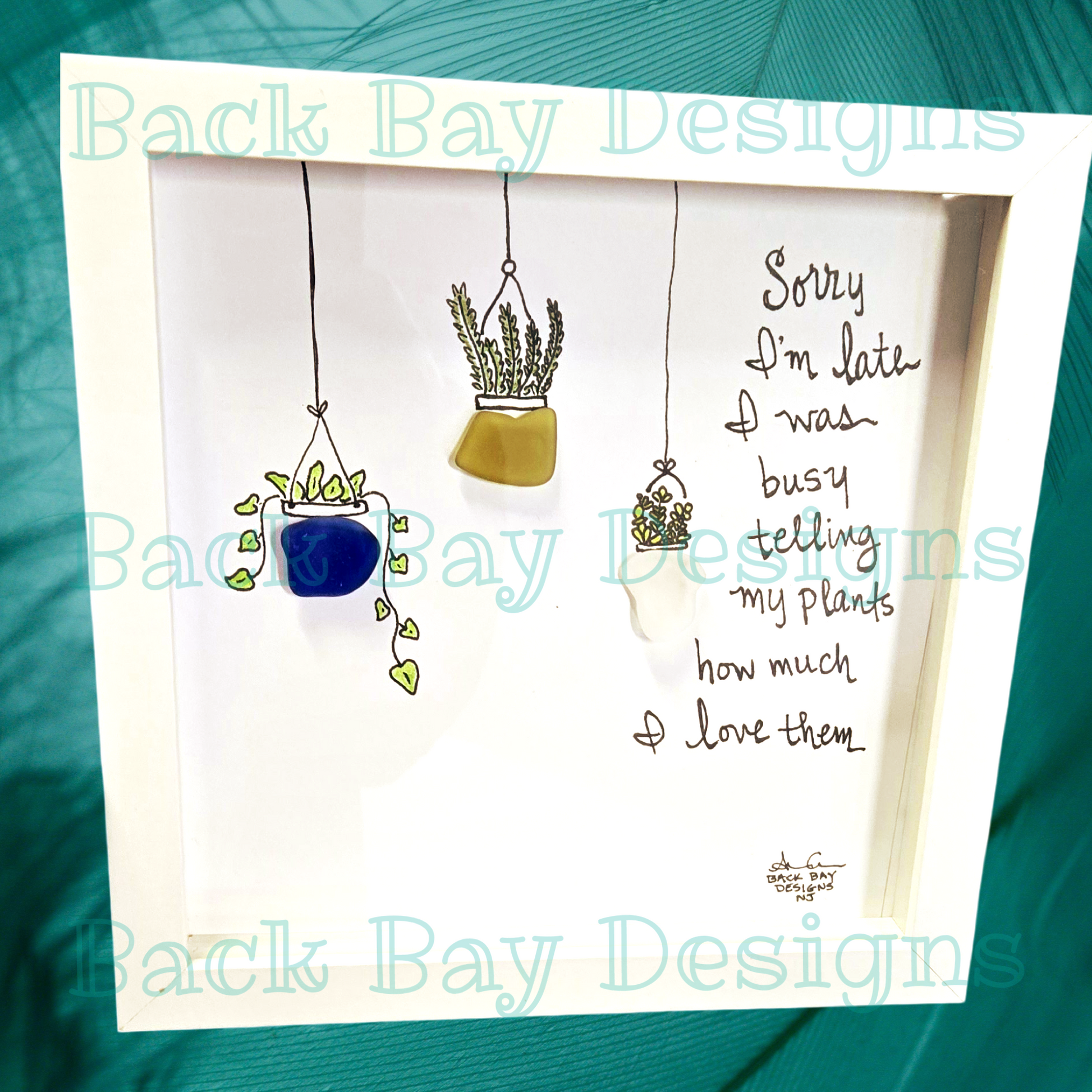 An 8 x 8 shadowbox frame with seaglass art, featuring a variety of seaglass plants and flowers, and the text 'Sorry I'm late I was busy telling my plants how much I love them'. sea glass art by back bay designs