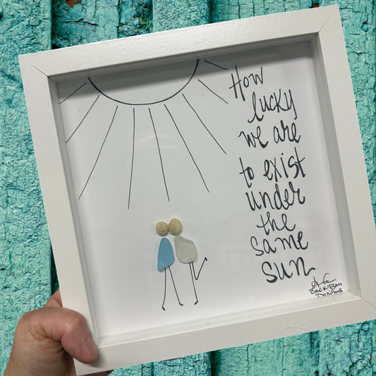 Framed artwork with a couple under a sun and text 'How lucky we are to exist under the same sun' sea glass art