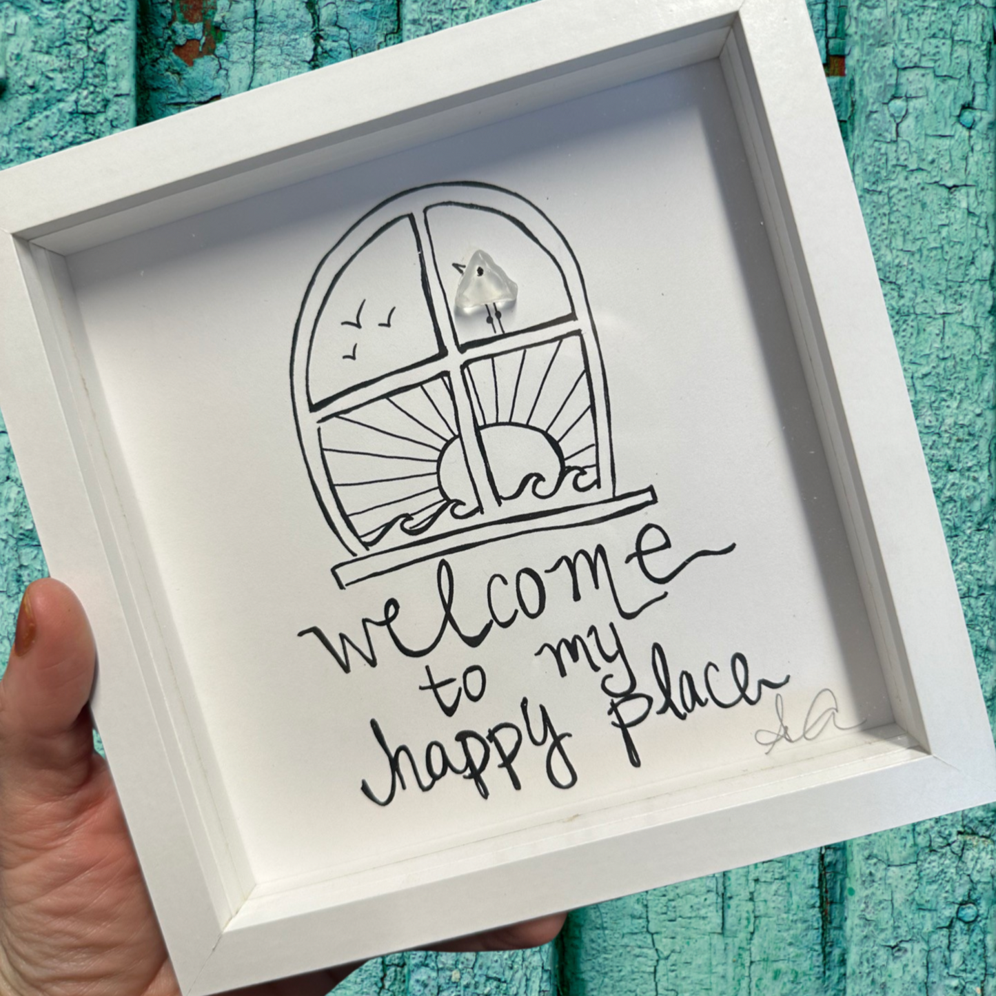 Framed artwork with 'welcome to my happy place' text and a window illustration on a textured teal background. Sea glass Art