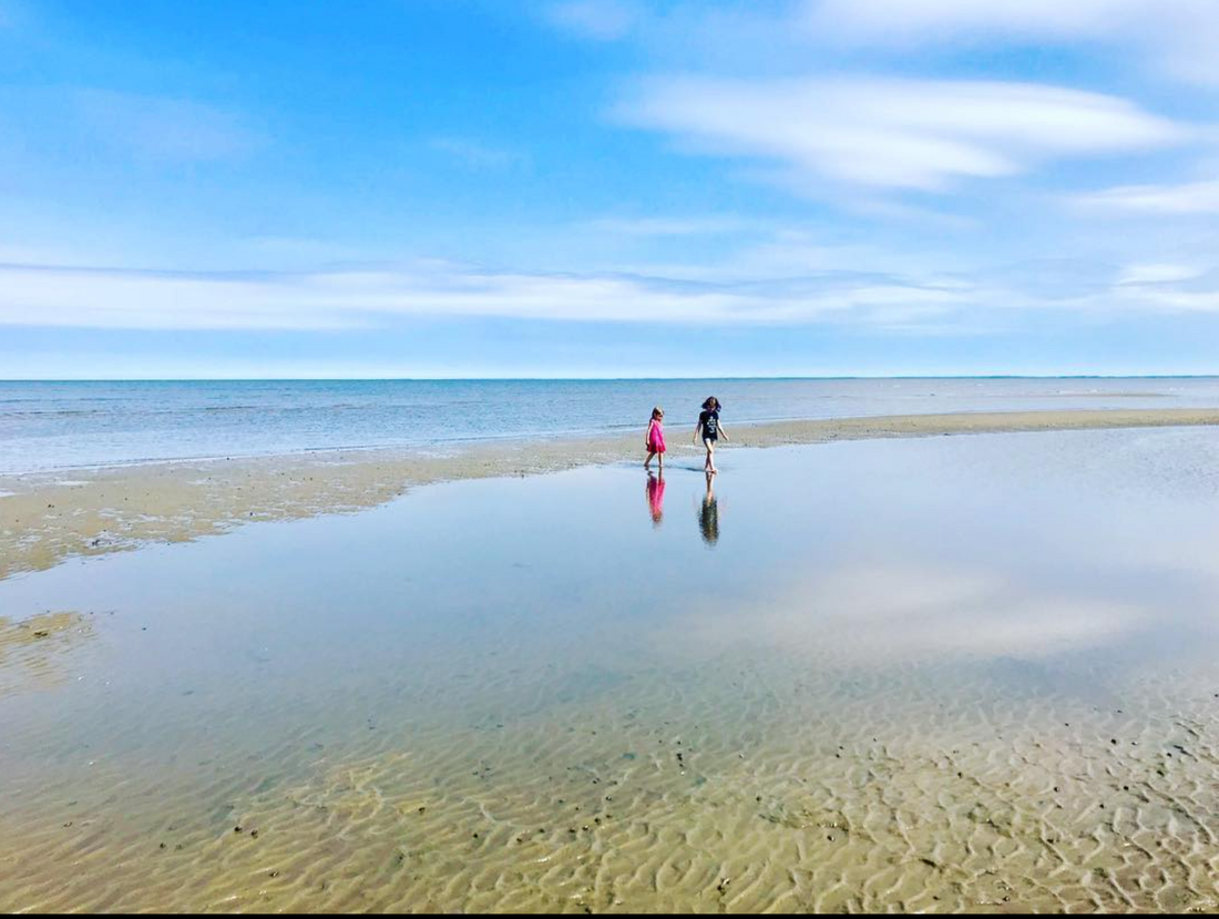 girls on sandbar in glassy bay reflecting sky 