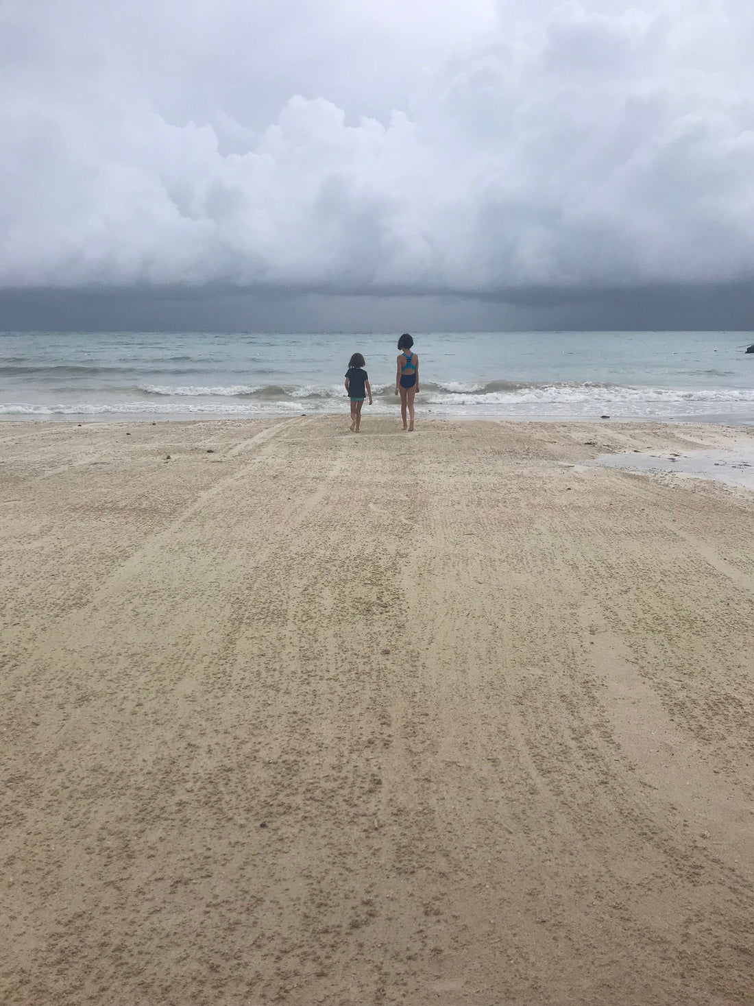 Small humans on a beach walking toward the shoreline and clouds 