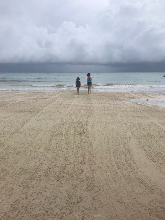 Small humans on a beach walking toward the shoreline and clouds 