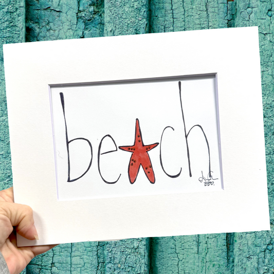 Hand holding a sign with 'beach' and a starfish against a teal wooden background
