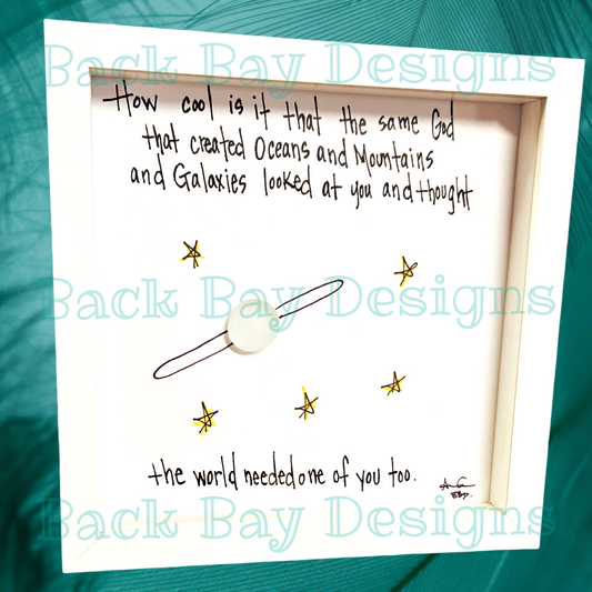 A 6x6 shadow box featuring plexiglass with a white background, stars, and text that reads 'How cool is it that the same God created oceans and mountains and galaxies and thought at you and me too?' Back Bay Designs is mentioned as the creator.