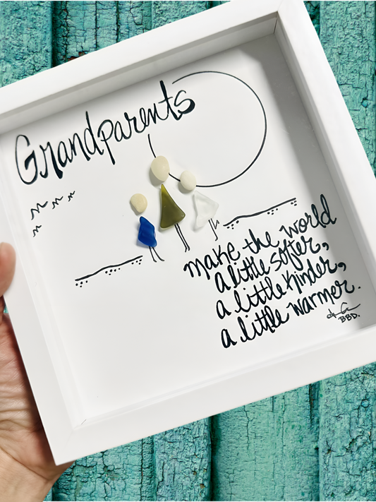 Decorative frame with 'Grandparents make the world a little softer, a little kinder, a little warmer' text and small figurines on a teal wooden background.