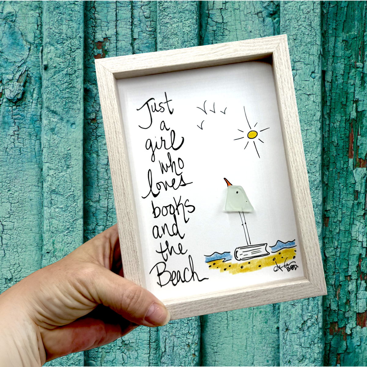 Quote: "Just a girl who loves books and the Beach" Image: Sea glass bird standing on a hand-drawn open book on a colorful shoreline with a sun and flying birds