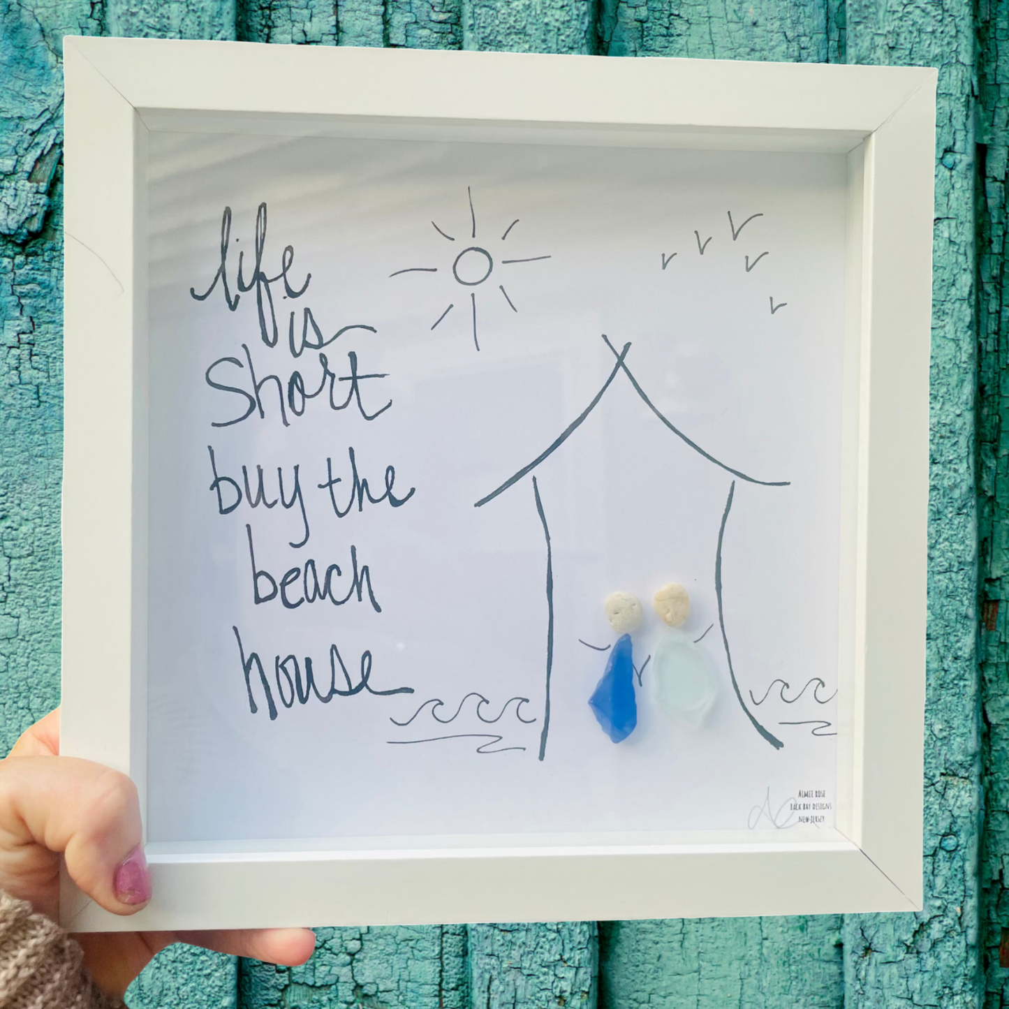 Framed artwork with 'Life is short, buy the beach house' text and illustrations against a textured teal background. Life is short buy the beach house 8in sea glass artwork 