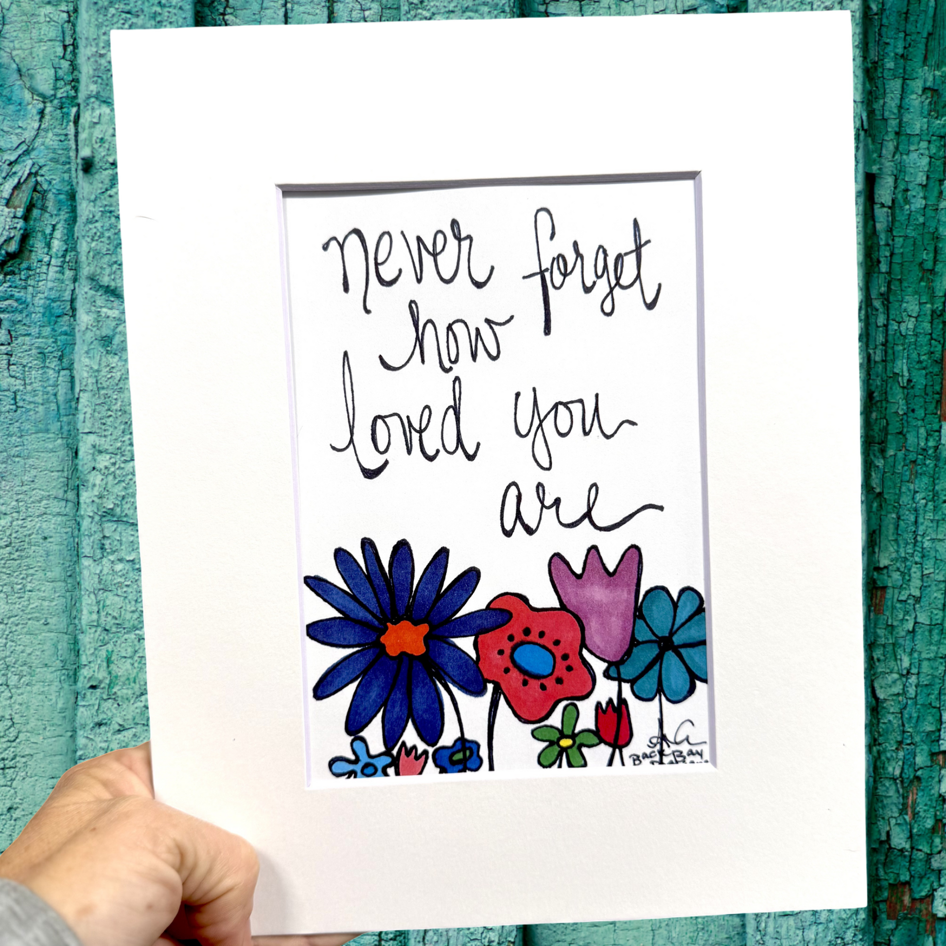 Hand holding a print with colorful flowers and text on a textured teal background