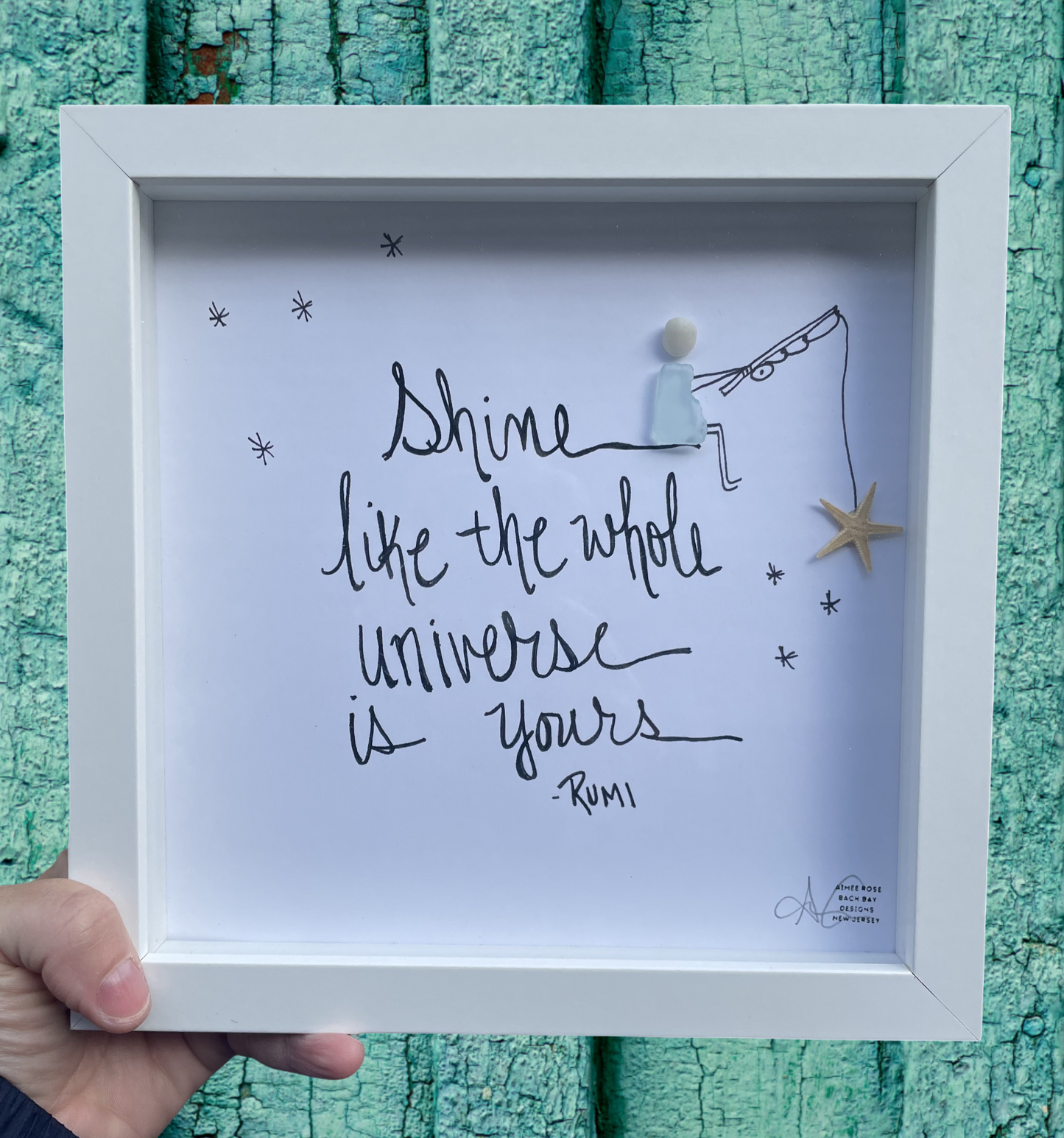 Framed artwork with 'Shine like the whole universe is yours' quote by Rumi on a textured teal background.