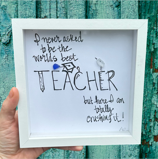 A 6x6 shadowbox with plexiglass, containing a piece of seaglass art with text that reads 'I NEVER ASKED TO BE THE WORLD'S BEST TEACHER, BUT HERE I AM, Totally Crushing  IT!'.
