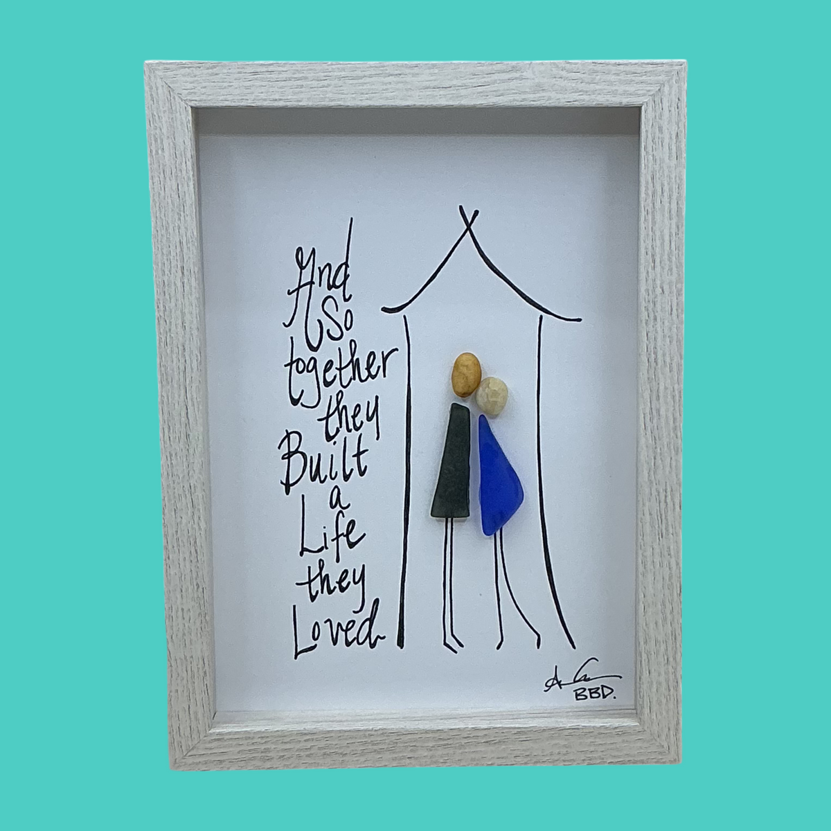 Quote: “And So together they Built a Life they Loved” Image: Two figures with pebble heads, sea glass bodies and hand-drawn legs leaning together inside a hand-drawn house outline