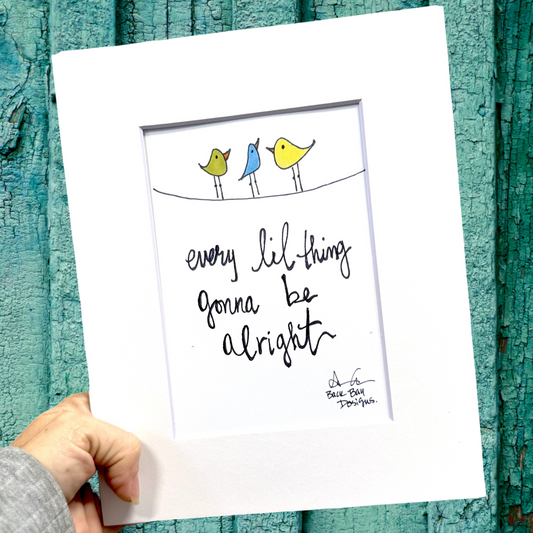 Hand holding a print with birds and 'every lil' thing gonna be alright' text against a textured teal background.