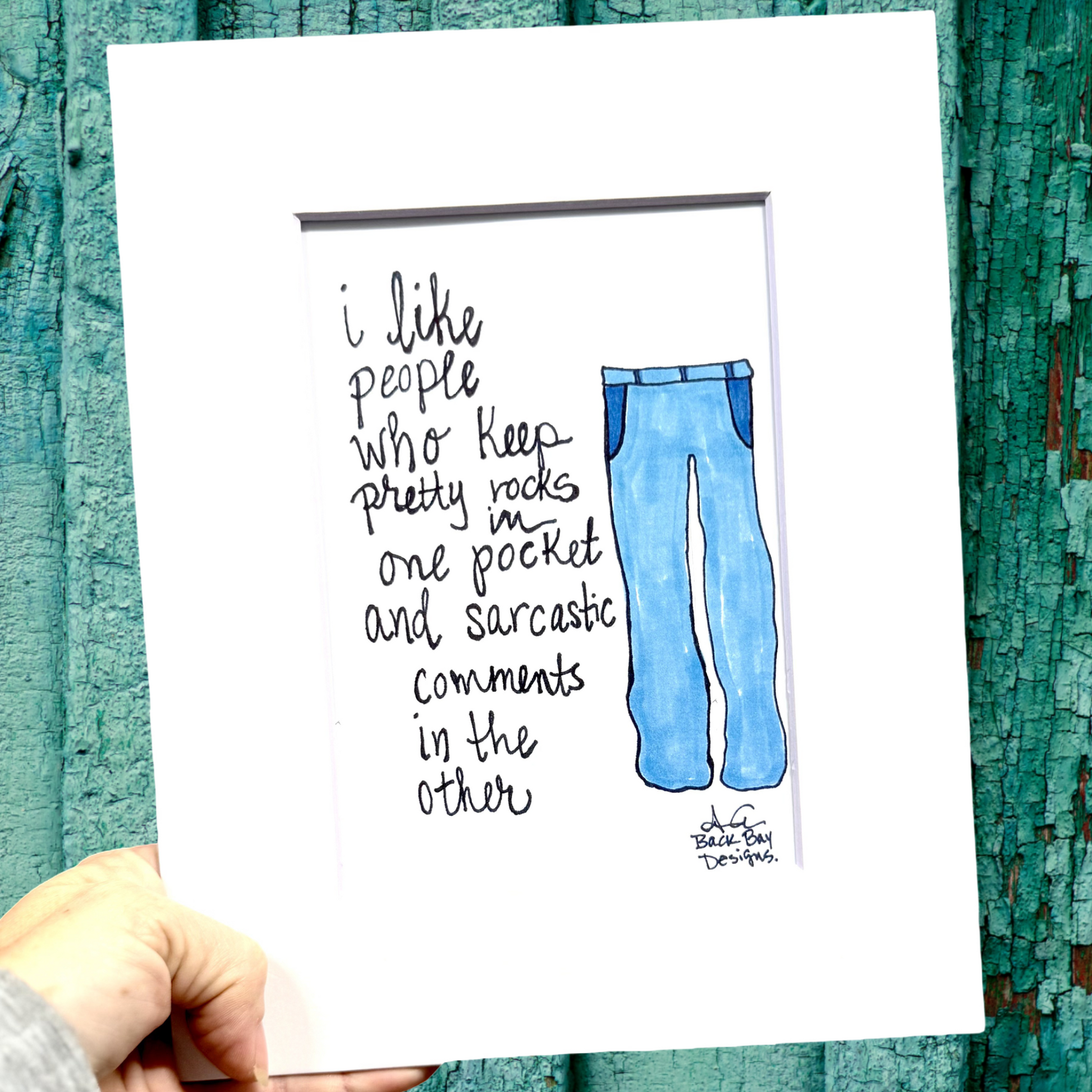 Hand holding a art print with blue jeans illustration and text against a textured teal background