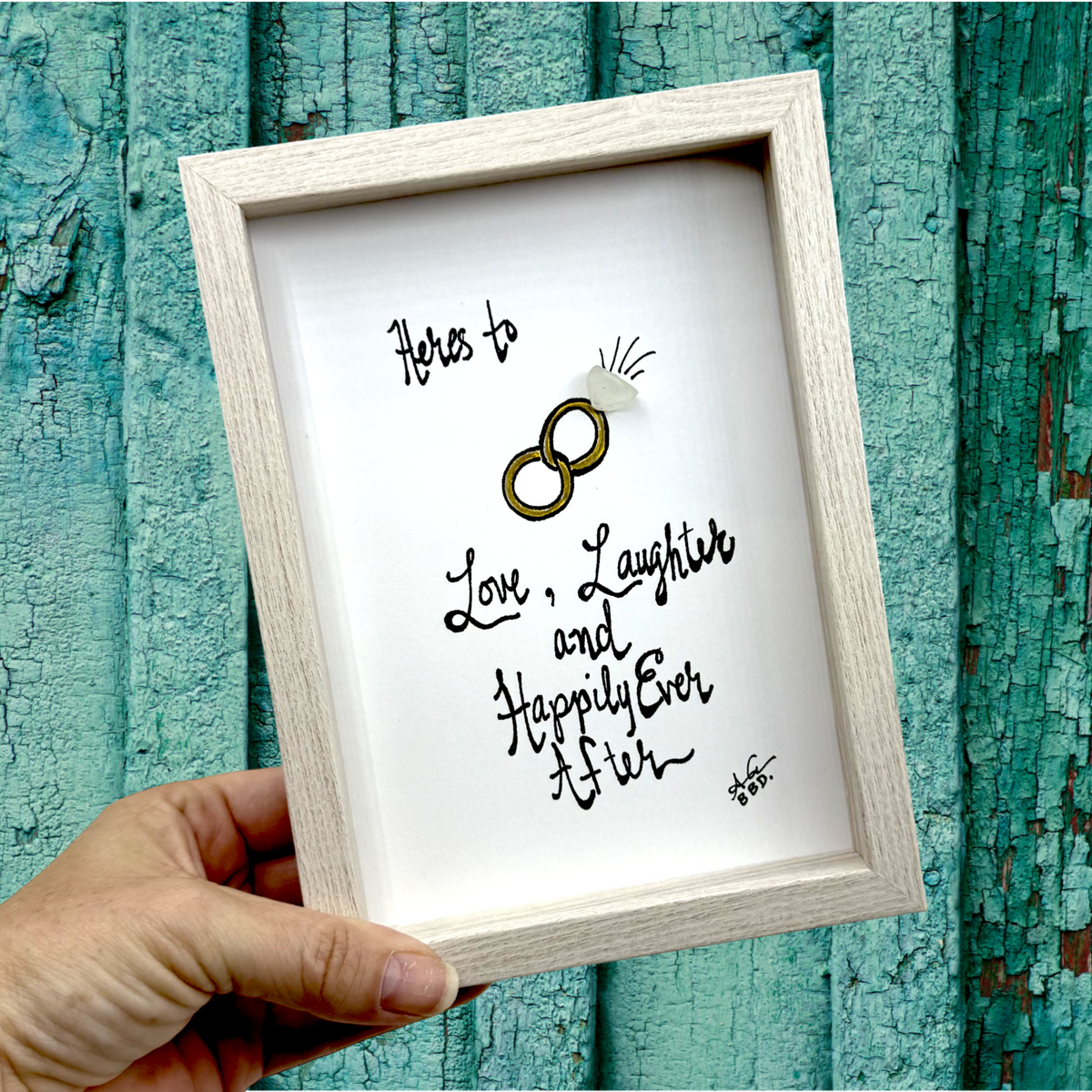 Quote: "Heres to Love, Laughter and Happily Ever After" Image: Two hand-drawn colorful interlocking wedding rings with a sea glass diamond