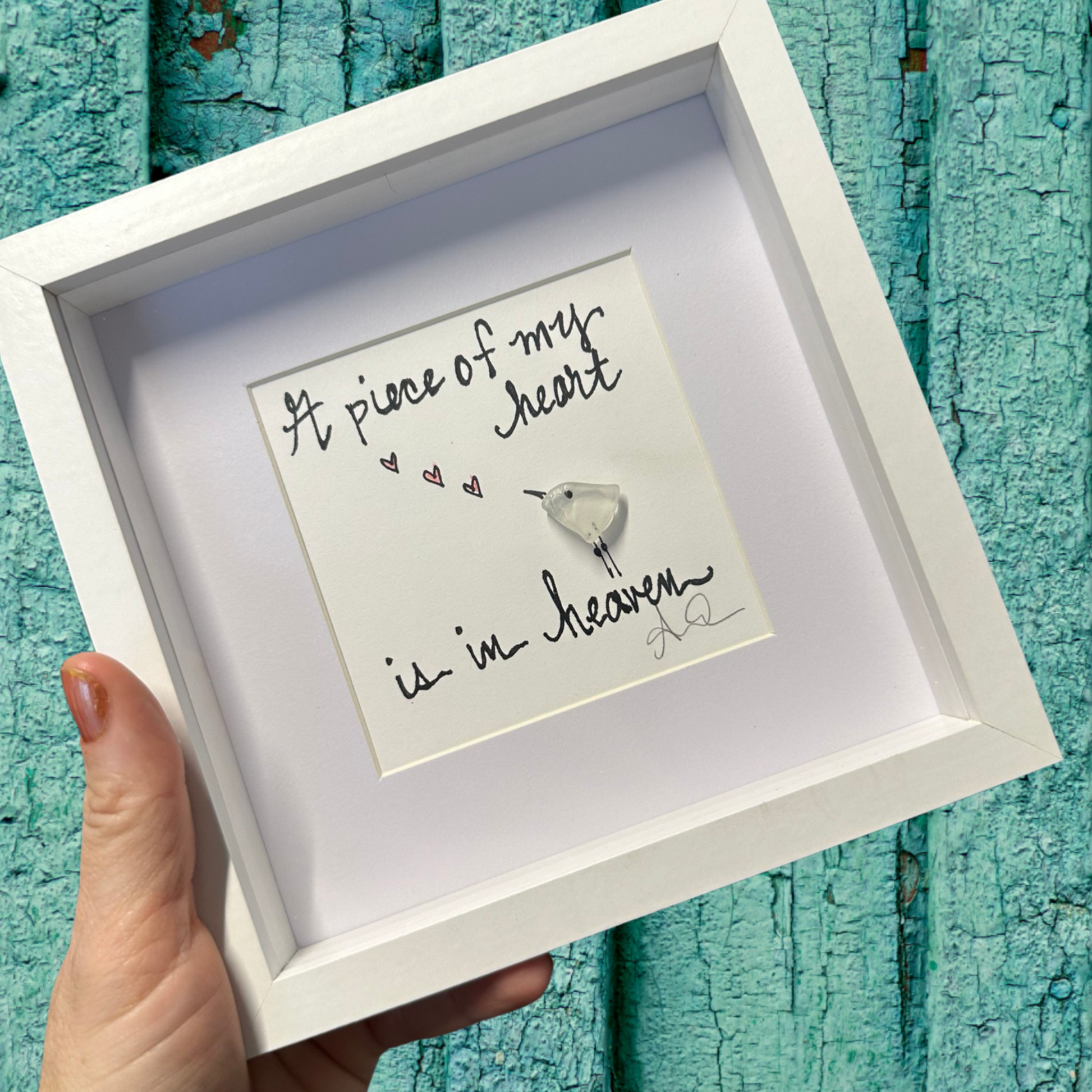 A 6x6 shadowbox frame made of plexiglass, containing a seaglass art piece with the text a piece of my heart is in heaven, little bird with hearts sea glass art 