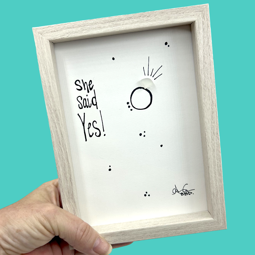 Quote: "She said Yes!" Image: Sea glass gem on a hand-drawn engagement ring with sparkle lines and scattered dots