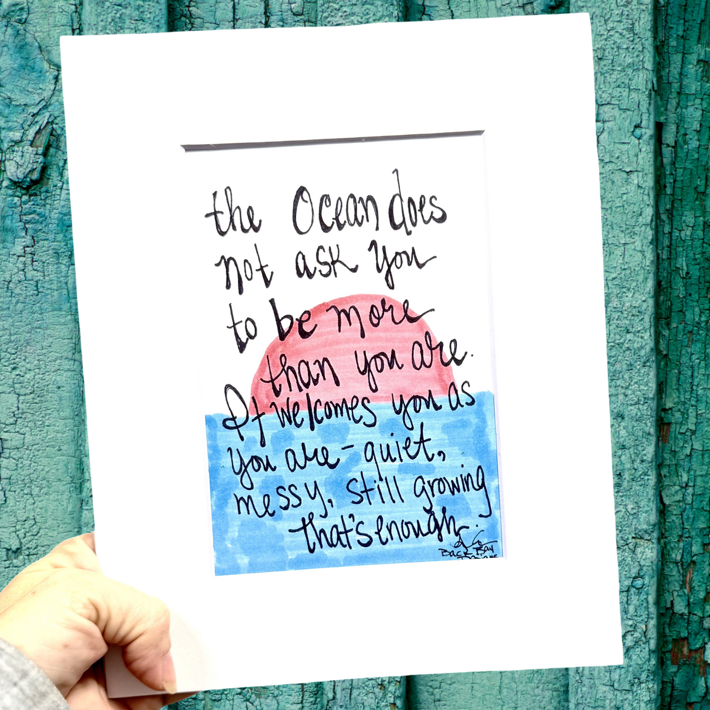 Handwritten quote on a print held against a textured teal background