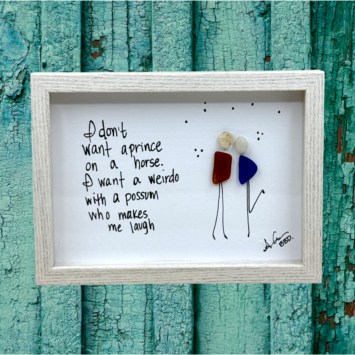 Quote: "I don't want a prince on a horse. I want a weirdo with a possum who makes me laugh" Image: Sea glass couple with pebble heads and hand-drawn stick bodies leaning in close, one kicking up a leg