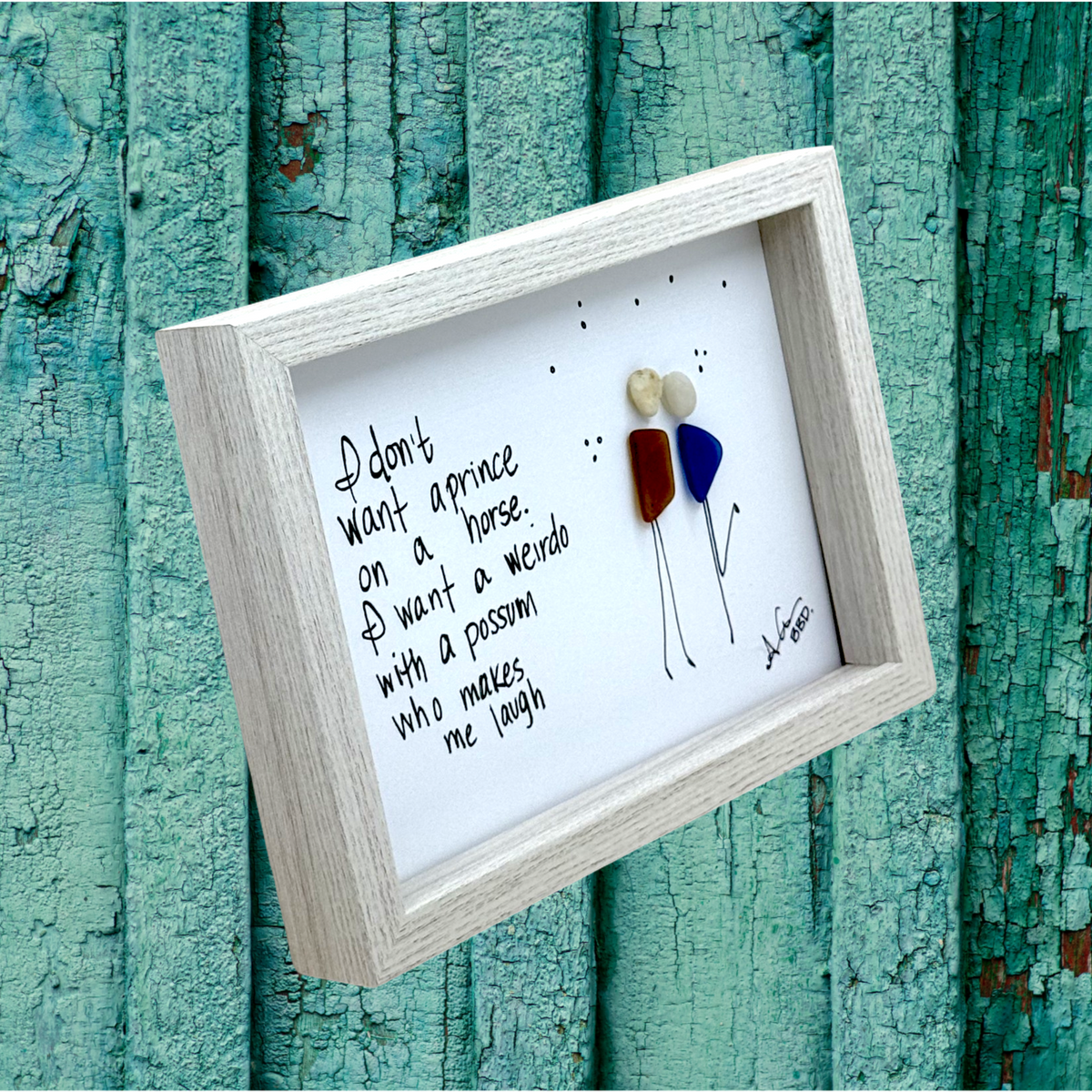 Quote: "I don't want a prince on a horse. I want a weirdo with a possum who makes me laugh" Image: Sea glass couple with pebble heads and hand-drawn stick bodies leaning in close, one kicking up a leg